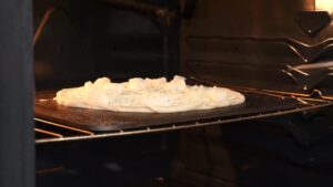 An unbaked white pizza is cooking on a hot pizza stone inside a preheated oven