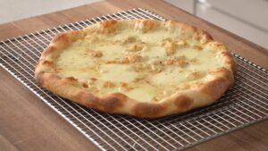 A freshly baked white pizza rests on a cooling rack with melted cheese and golden-brown crust