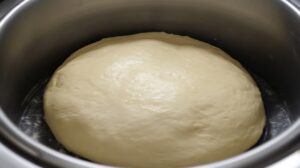 Risen pizza dough in a stainless steel bowl after proofing