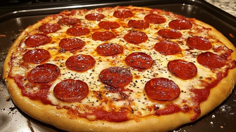 Homemade pepperoni pizza on a baking tray, topped with melted cheese and sliced pepperoni