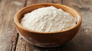 A wooden bowl filled with white flour on a rustic wooden table