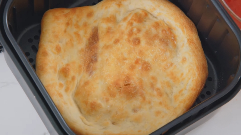 A golden, crispy pizza dough base in an air fryer before adding toppings