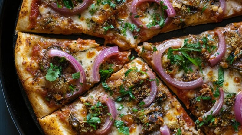 Close-up of pizza slices topped with pickled mackerel, red onion rings, herbs, and melted cheese