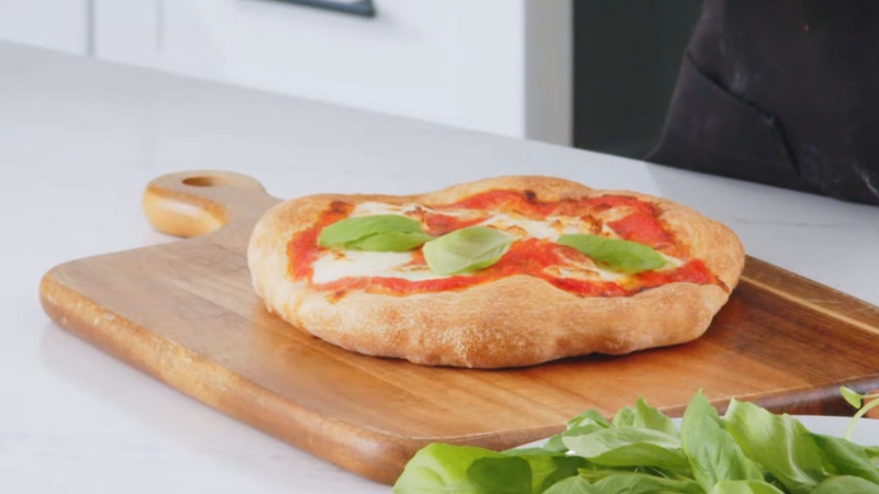 A freshly baked pizza with basil leaves on top, placed on a wooden pizza board