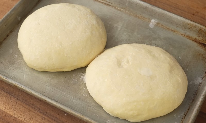 Two smooth, pale dough balls resting on a well-used, rustic metal baking sheet