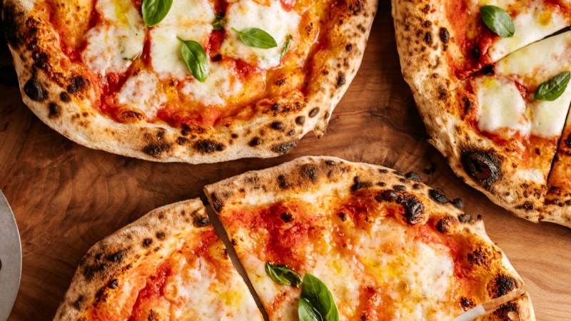 Wood-fired pizzas topped with fresh mozzarella and basil, sliced and ready to serve on a rustic wooden table