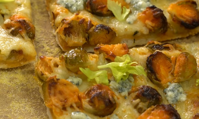 A pizza topped with melted cheese, fresh vegetables, and aromatic herbs