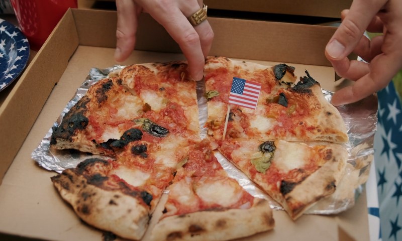 A pizza featuring an American flag is being lifted out of a box